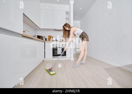 Ampio angolo di pulizia pavimento casalinga giovane in appartamento, lavaggio macina piano cucina con mop umido e detergente, femmina che fa la casa chor Foto Stock