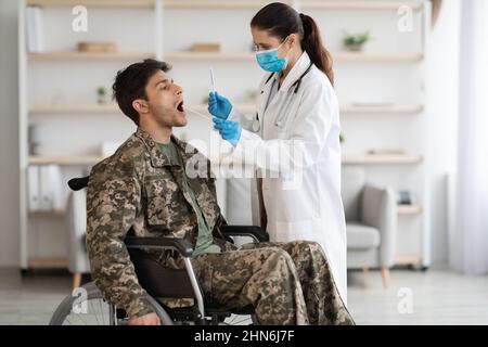 Il medico preleva un campione per il test PCR dal soldato in sedia a rotelle Foto Stock