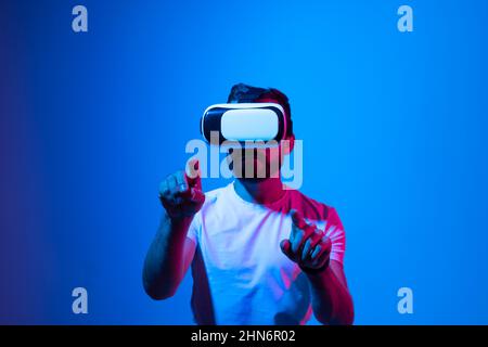 L'uomo eccitato sperimenta la realtà virtuale tramite visore VR e tocca qualcosa, allunga e zooma con le mani. Foto Stock