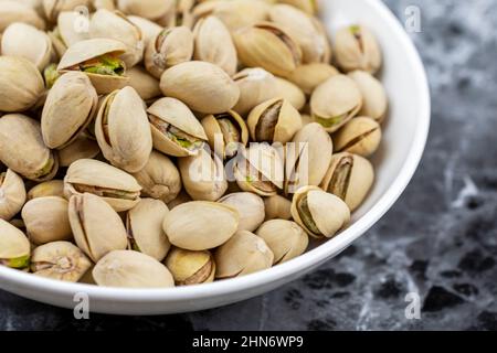 Vista laterale di una ciotola bianca di pistacchi su una superficie di marmo nero. Foto Stock