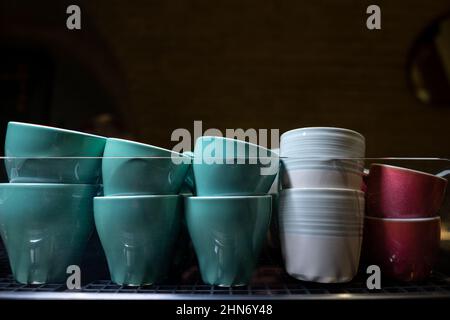 set di tazze o tazze in ceramica colorate riscaldanti su macchina da caffè professionale Foto Stock