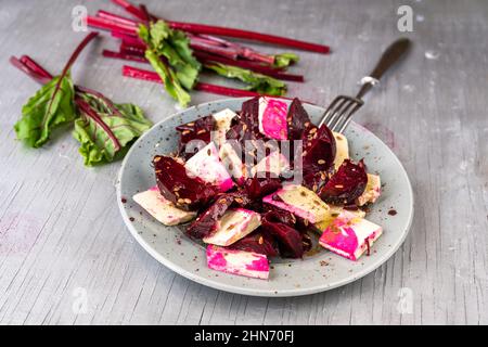 Cibo vegetariano o vegano, tofu con barbabietola rossa al forno sul piatto, forchetta e foglia verde sul tavolo, primo piano. Foto Stock