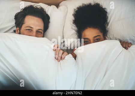 Indovinate cosa si nascondeva. Ritratto ad angolo alto di una giovane coppia affettuosa che si copre giocosamente con una coperta nella loro camera da letto a casa. Foto Stock