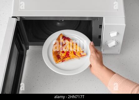 Donna mettere piatto con pezzo di pizza in forno a microonde sul tavolo, primo piano Foto Stock