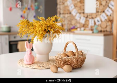 Coniglio di Pasqua, cestino di uova e vaso con fiori di mimosa sul tavolo da pranzo Foto Stock