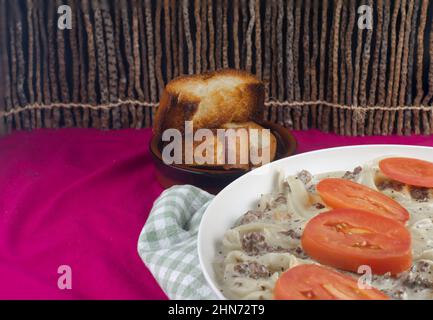 Carne macinata di manzo e pasta con salsa all'aglio, pane all'aglio e pomodoro a fette su lino rosso, fondo di legno di bastone, Foto Stock