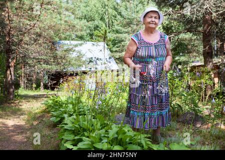 Donna giardiniere anziana che lavora nella sua fattoria e sorridente, ritratto a tutta lunghezza con potatrice giardino nelle sue mani Foto Stock