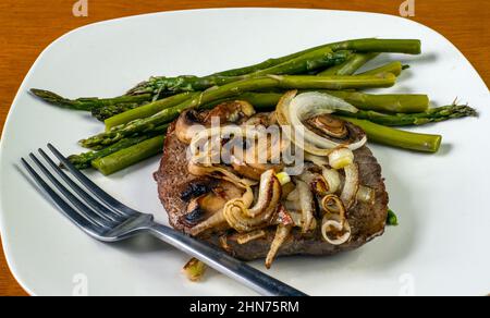 una bistecca con cipolle saltate e funghi con asparagi Foto Stock