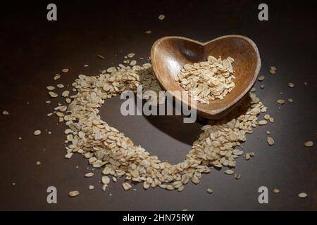 Mucchio di fiocchi d'avena a forma di cuore. Cuore di farina d'avena su sfondo scuro. Mangiare sano Foto Stock