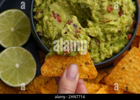 Vista dall'alto della mano con gustose tortilla chips o nachos con salsa guacamole fresca fatta in casa Foto Stock