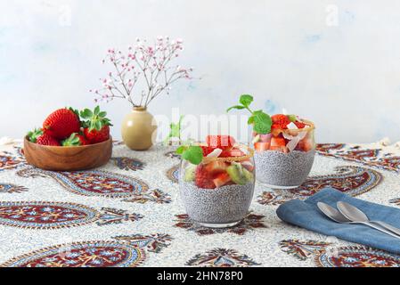 Vista ad angolo basso del dessert chia budino con bacche estive, fragole, kiwi e fette di cocco, impreziosito da un rametto di menta. Nessuna gente. Foto Stock