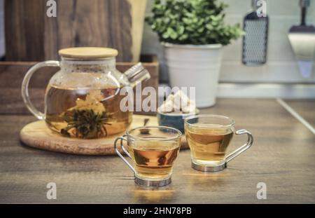 Tè fiorito in teiera di vetro e due tazze sul piano di lavoro della cucina Foto Stock