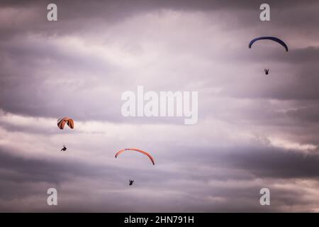 Immagine di alcuni parapendio che volano, contro un cielo grigio nuvoloso. Foto Stock