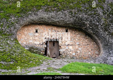 Un'antica dimora sotto una collina ricoperta di erba e vegetazione al centro, una vecchia porta e due piccole finestre. Architettura antica. Antica casa Foto Stock