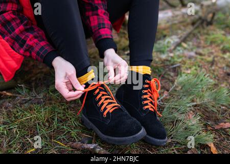 La ragazza è seduta su un ceppo nella foresta e legando scarpe luminose. Concetto di viaggio, trekking ed escursionismo Foto Stock