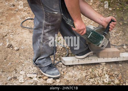 Operaio di costruzione con sega elettrica che taglia mattoni di pavimentazione Foto Stock