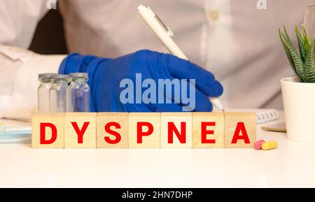 La parola DISPNEA è scritta su cubi di legno vicino ad uno stetoscopio su sfondo di legno. Concetto medico Foto Stock