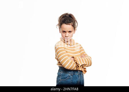 Giovane ragazza che guarda arrabbiata alla macchina fotografica mentre si posa con le braccia incrociate su uno sfondo isolato. Foto Stock