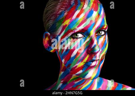 Creatività con i colori. Studio girato di una giovane donna in posa con vernice colorata sul suo volto su uno sfondo nero. Foto Stock