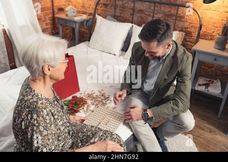 parenti, nonna e il suo più antico nipote che giocano enigmi di vocabolario insieme nella sua camera da letto. Foto di alta qualità Foto Stock