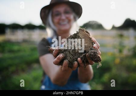 Primo piano di donne più career mani che tengono terreno all'aperto in fattoria di comunità. Foto Stock