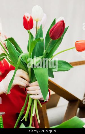 Donna fiorista fa bouquet di tulipani freschi. Fiori di primavera in negozio di fiori. Piccola impresa per giardinieri. Piante crescenti in serra. Foto Stock