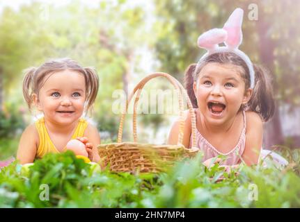 I bambini della sorella si trovano sull'erba con un cestino e le uova di Pasqua nel cortile Foto Stock