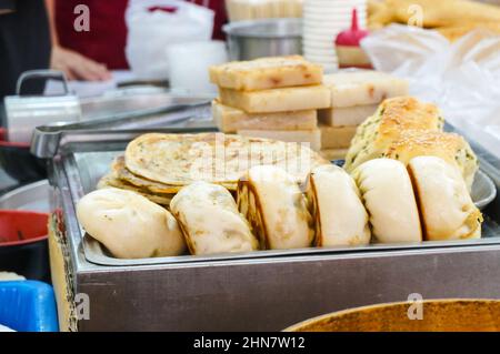 Concentratevi sui tradizionali panini di carne fritti in padella presso un mercato all'aperto a Kaohsiung, Taiwan, e su una varietà di piatti taiwanesi per la colazione in background come Foto Stock