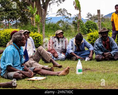 Gli anziani del Papuan seduti sull'erba durante un incontro di comunità, ascoltando attentamente l'oratore Foto Stock