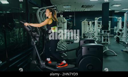 Adatta la donna atletica che si esercita su una macchina ellittica. Allenamento di attività femminile muscolare in palestra moderna. Sport persone allenarsi in un ellittico Walking Trainer Fitness. Movimento lento dell'esercizio Foto Stock