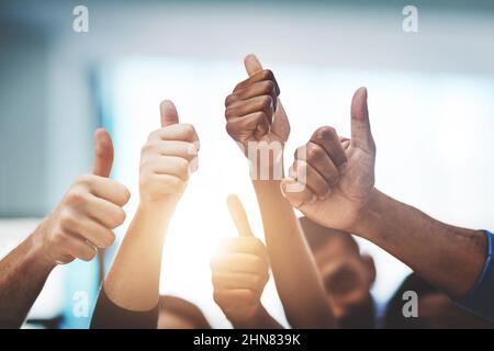 Continuate a lavorare in modo straordinario. Scatto ritagliato di un team di colleghi che mostra i pollici al lavoro. Foto Stock