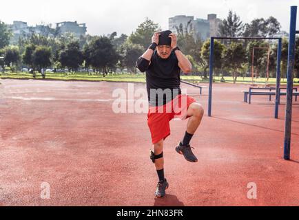 Un atletico latino che corre al suo posto riscaldandosi per l'esercizio sportivo all'aperto in un parco Foto Stock