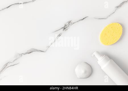 Schiuma detergente viso flacone aperto con campione di schiuma e spugna per la pulizia del viso su sfondo di marmo. Vista dall'alto, piatto. Spazio di copia Foto Stock