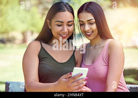 Scopri le ultime novità sui social media. Scatto ritagliato di due giovani amici utilizzando un cellulare esterno. Foto Stock