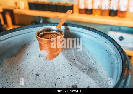 Cucinare caffè fresco in cezve su sabbia calda secondo una tradizione antica Foto Stock