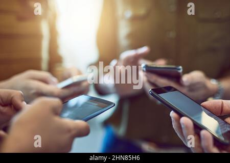 Rimanere connessi = mantenere la corrente. Scatto ritagliato di un gruppo di colleghi che utilizzano i loro smartphone in sincronia. Foto Stock