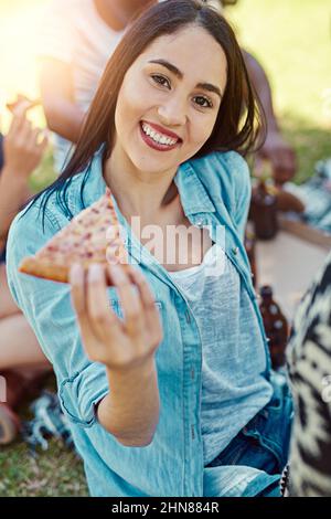 La pizza è l'unico triangolo d'amore che voglio. Ritratto di una giovane donna che mangia pizza mentre fuori su un pic-nic con gli amici. Foto Stock