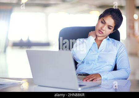 Il mio collo mi uccide. Shot di una giovane donna d'affari che soffre di dolore al collo mentre si siede alla sua scrivania. Foto Stock