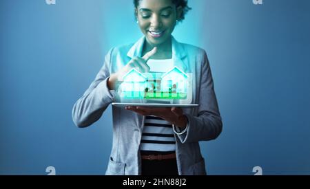 La tua casa perfetta è a portata di app. Studio girato di una giovane donna d'affari utilizzando un tablet digitale con grafica di proprietà su sfondo blu. Foto Stock