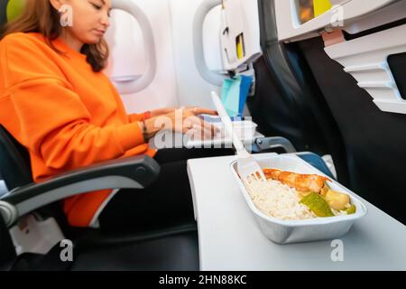 La donna felice ha ordinato gustoso piatto durante il volo in aereo e mangia pesce con riso. Catering e menu sull'aeroplano Foto Stock