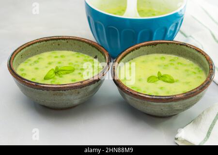 Zuppa di sedano cremosa con piselli verdi e basilico fresco da vicino in ciotole su sfondo di marmo grigio chiaro Foto Stock