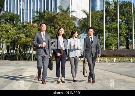 gruppo di quattro giovani uomini d'affari asiatici che camminano all'aperto in strada nella città moderna Foto Stock