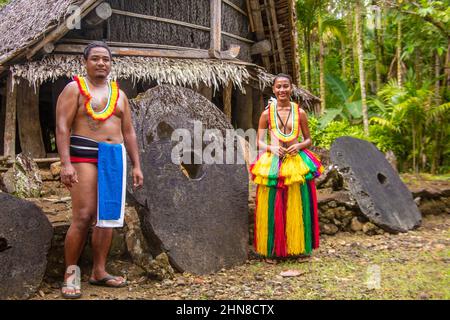 Questa coppia (MR) è in abiti tradizionali per cerimonie culturali e stare accanto a soldi di pietra in un villaggio sull'isola di Yap, Micronesia. Foto Stock