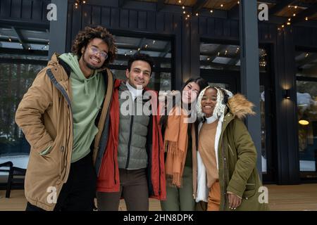 Ritratto di amici felici che si abbracciano e sorridono a macchina fotografica mentre si trova all'aperto con bella villa sullo sfondo Foto Stock