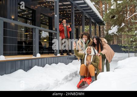 Gruppo di amici che si divertono slittino sulla slitta durante le vacanze invernali vicino alla loro casa di campagna all'aperto Foto Stock