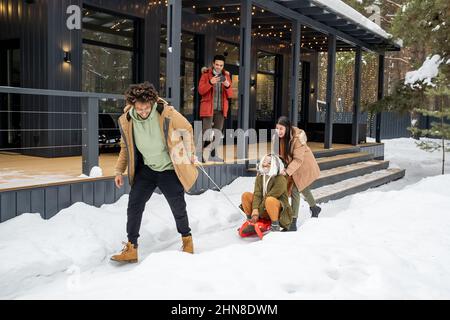 Gruppo di amici giocosi che dormono insieme sulla neve mentre riposano nella casa di campagna durante le vacanze invernali Foto Stock