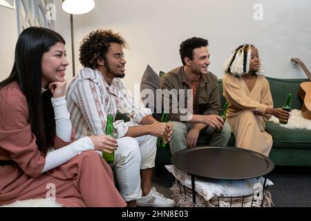 Amici giovani felici seduti sul divano ridendo e bevendo birra mentre guardate il divertente film a casa Foto Stock