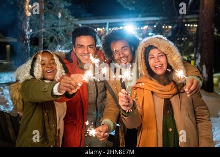 Ritratto di amici felici sorridenti a macchina fotografica in piedi all'aperto con scintille nelle loro mani e divertirsi durante le vacanze invernali Foto Stock