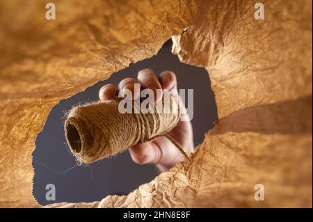 Una mano inserisce uno spago in un sacchetto di carta marrone. La mano di un uomo maturo tiene il filo di iuta. Scatto dal basso verso l'alto. Primo piano. Messa a fuoco selettiva. Foto Stock