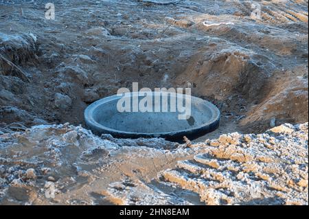 Anello di calcestruzzo per un pozzo d'acqua nel terreno congelato. Nel foro scavato è presente un prodotto ferro-calcestruzzo. Lo strato superiore di terreno è coperto con fr Foto Stock